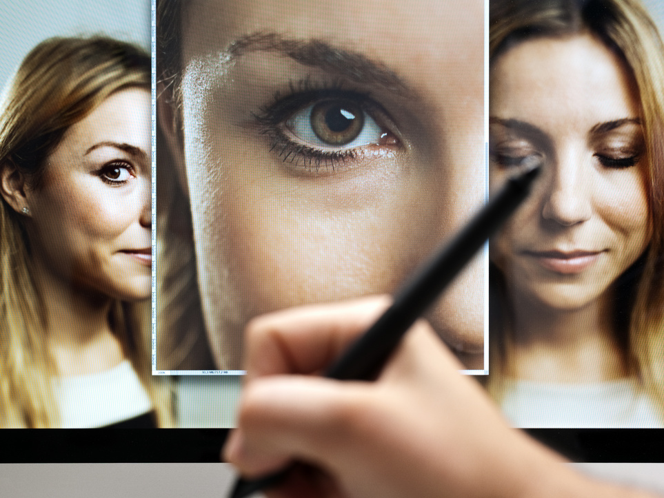 A person holding a graphic design pen in front of a computer screen editing a photo.